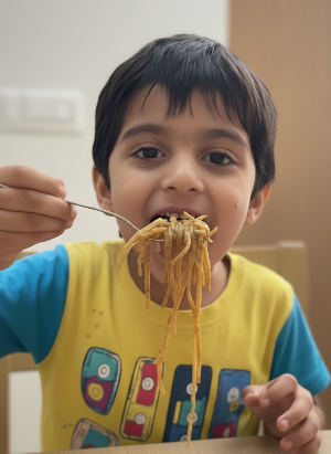 Child eating thi-thi noodles with a fork at a table